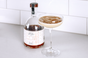 Maple Gin Flip cocktail in coupe glass with a bottle of Miss Maple